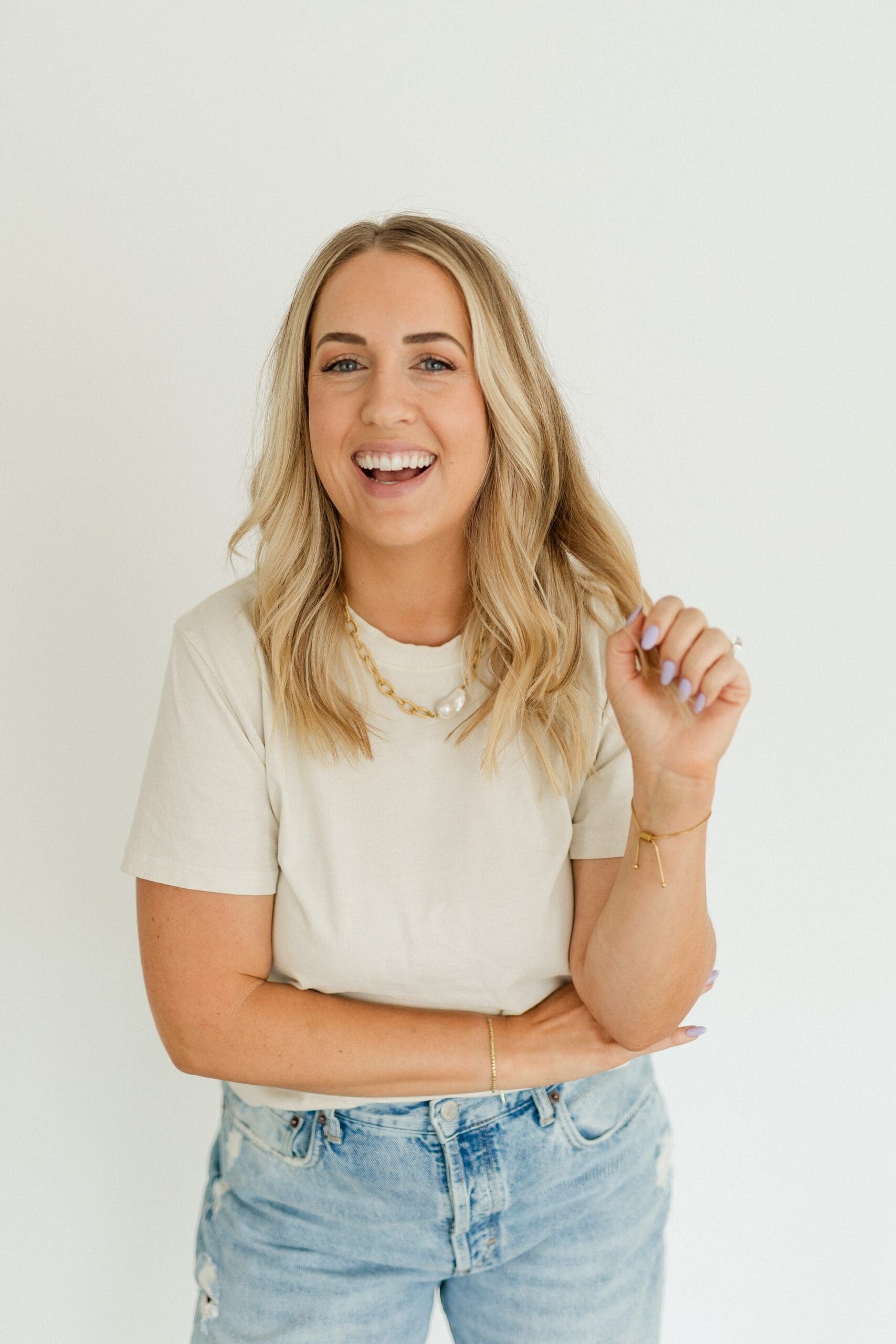 blonde girl smiling in white tshirt and gold necklack, light jeans